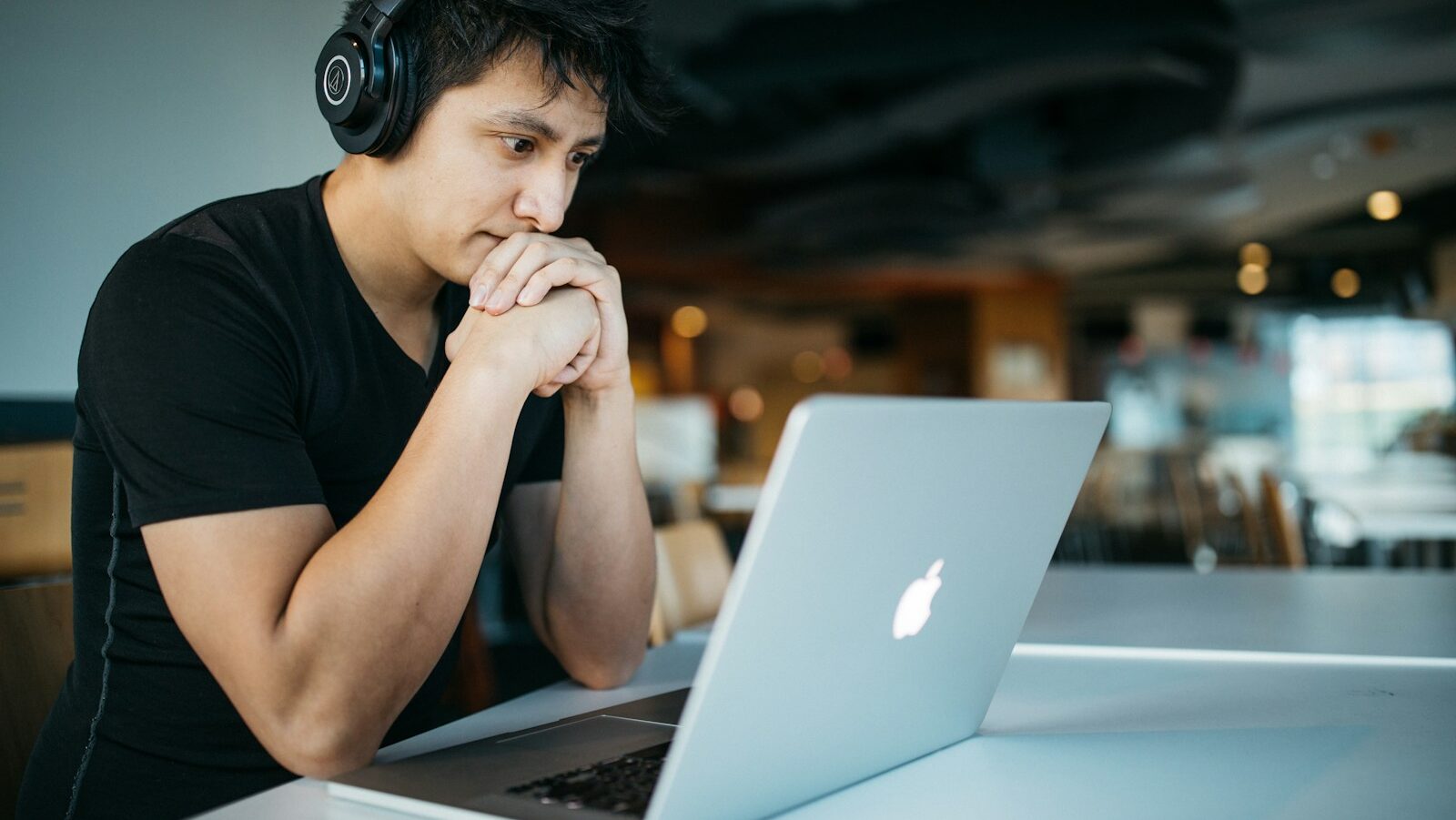 man wearing headphones while sitting on chair in front of MacBook